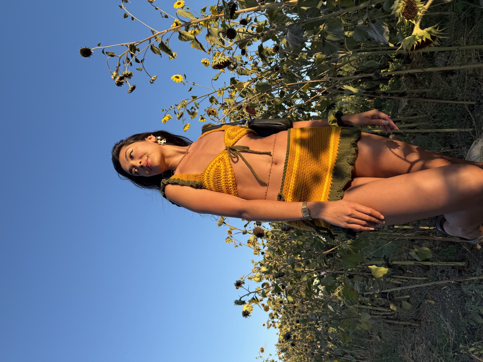 Woman in the mustard crochet set gazing up, sunflower field behind her