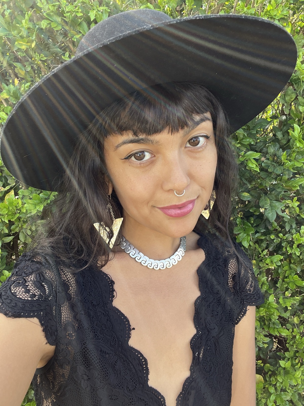Portrait wearing a wide-brim hat, a hammered silver collar necklace, and the same garnet triangle earrings