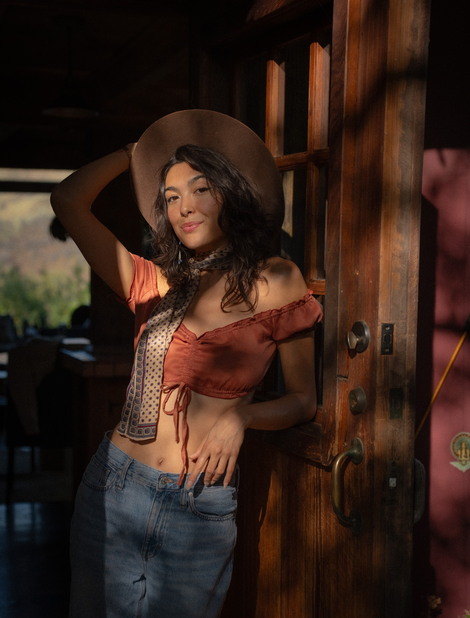 Gemma Rose leaning in a rustic wooden doorway, golden hour light