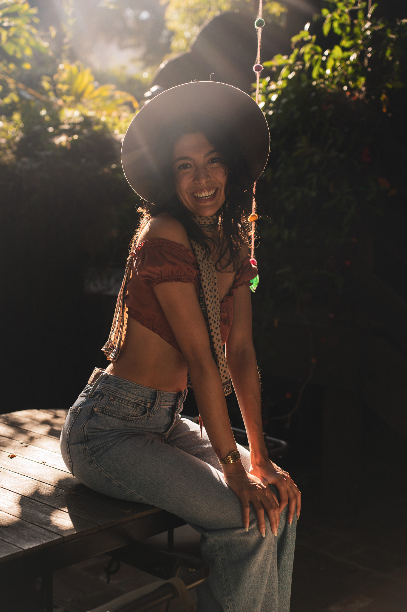 Gemma Rose laughing in dappled golden light, wearing a wide-brim hat