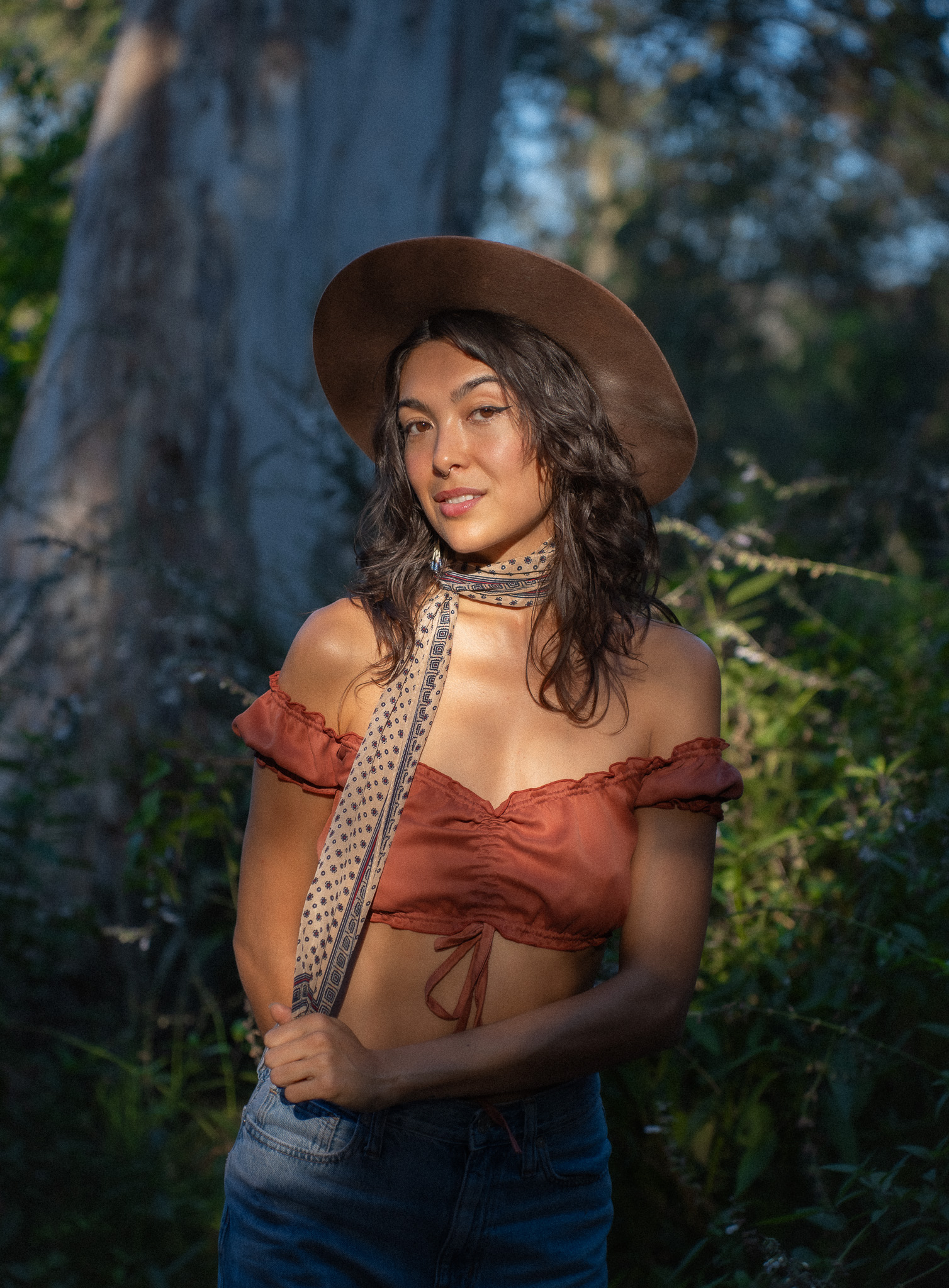 Gemma Rose in a wide-brim hat and rust off-shoulder top, golden hour in the trees