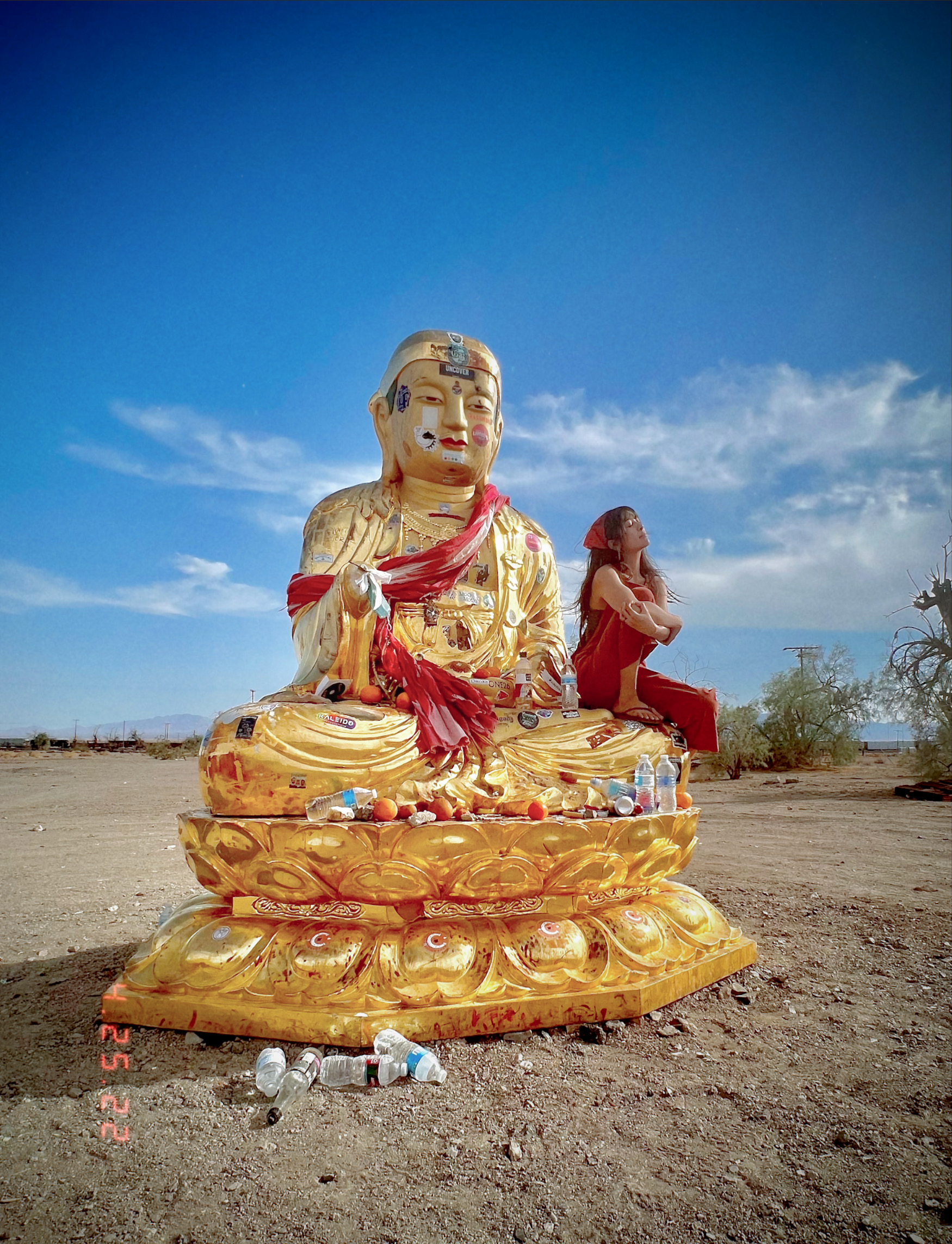 Gemma Rose sitting beside a sticker-covered golden Buddha statue in the desert